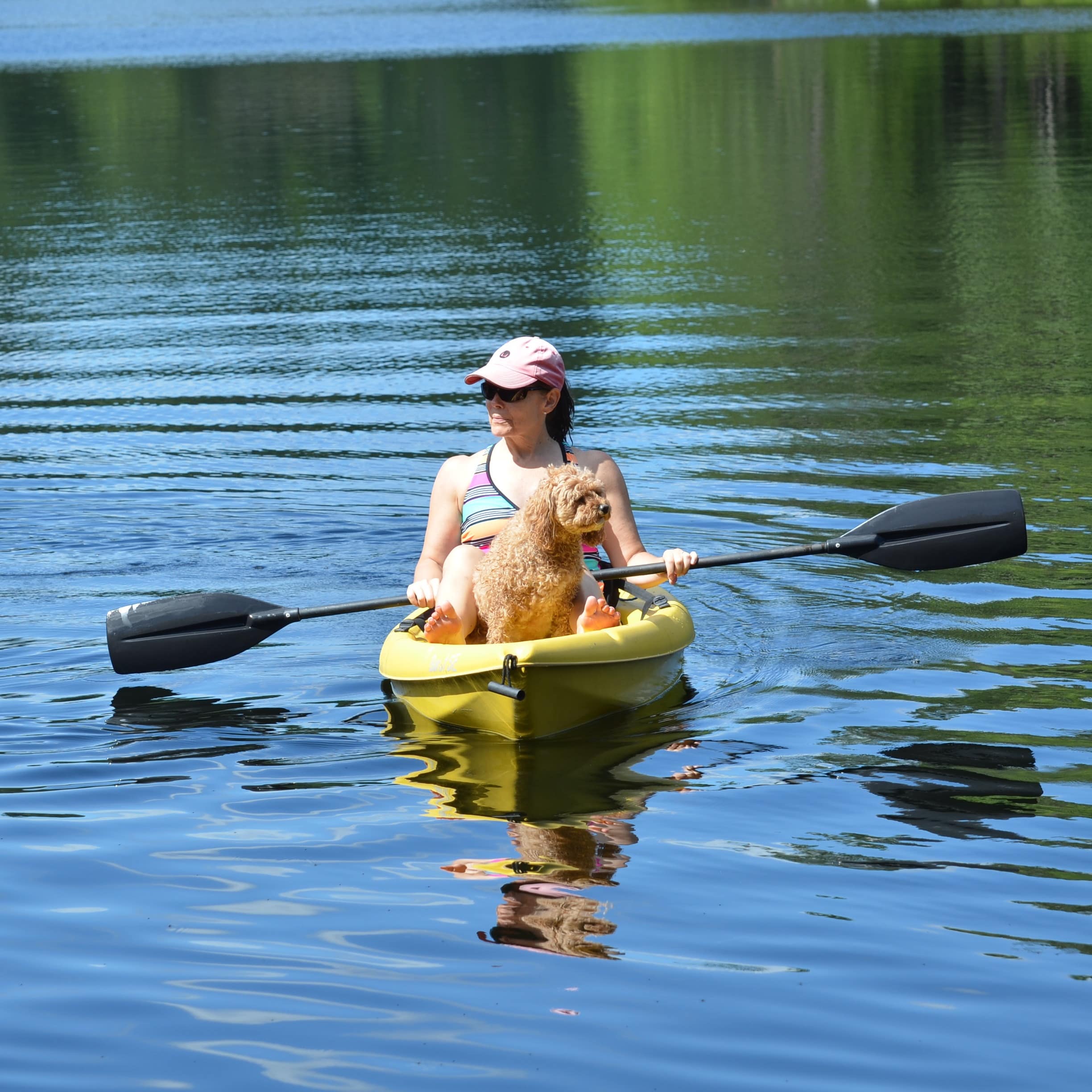 A woman holding a paddle and sitting with a brown dog in a yellow kayak in a river