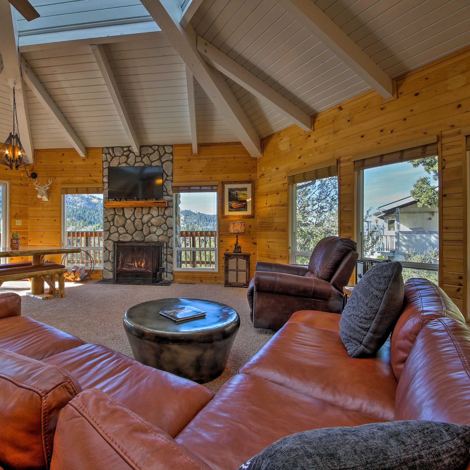 Leather recliner and couches around fireplace in airy lounge with deck access and mountain views