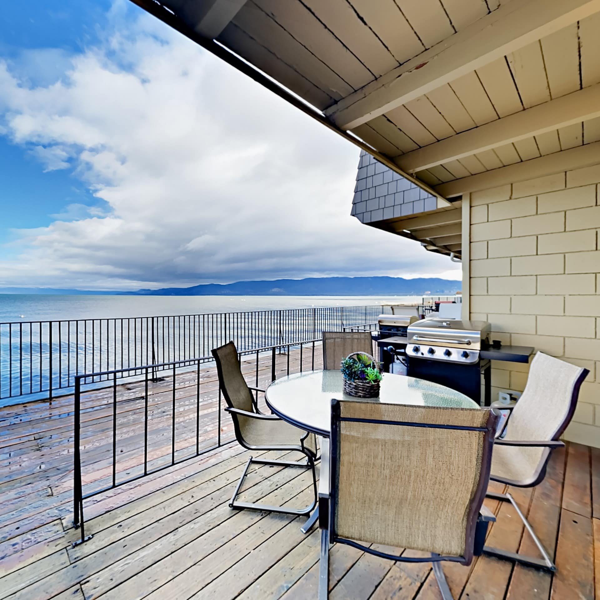 An outdoor dining table by a grill on a deck overlooking the lake