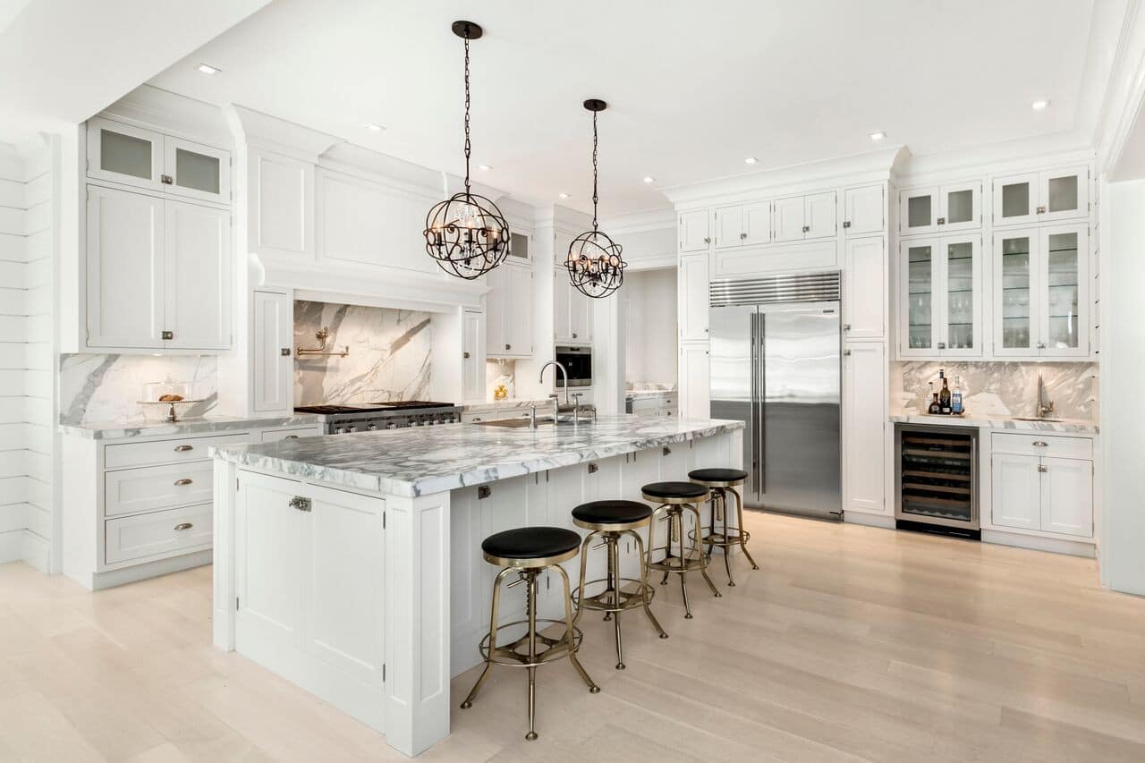 This is a white and marble kitchen with metal accent lighting and bar stools.