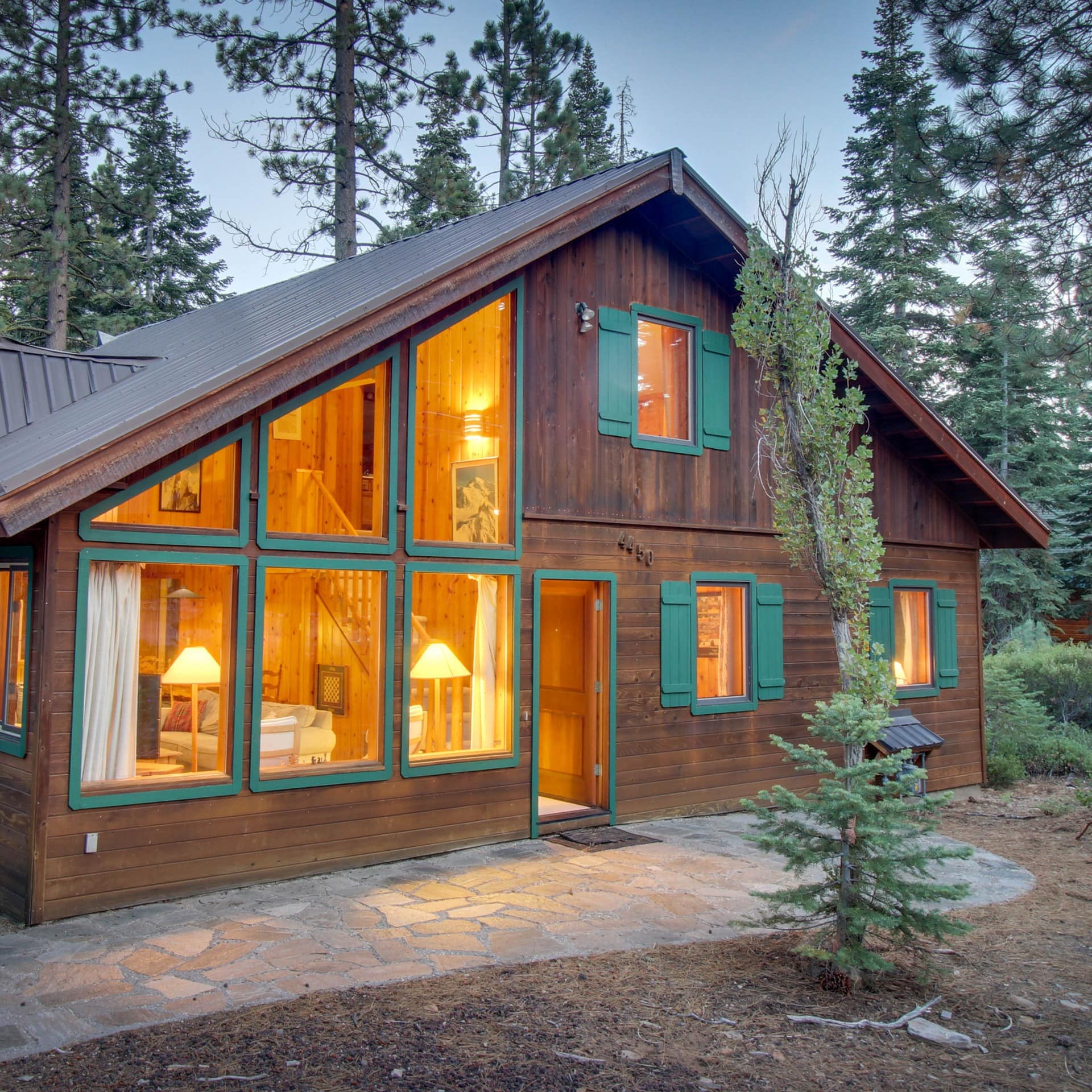 A rustic chalet lit from the interior and surrounded by trees