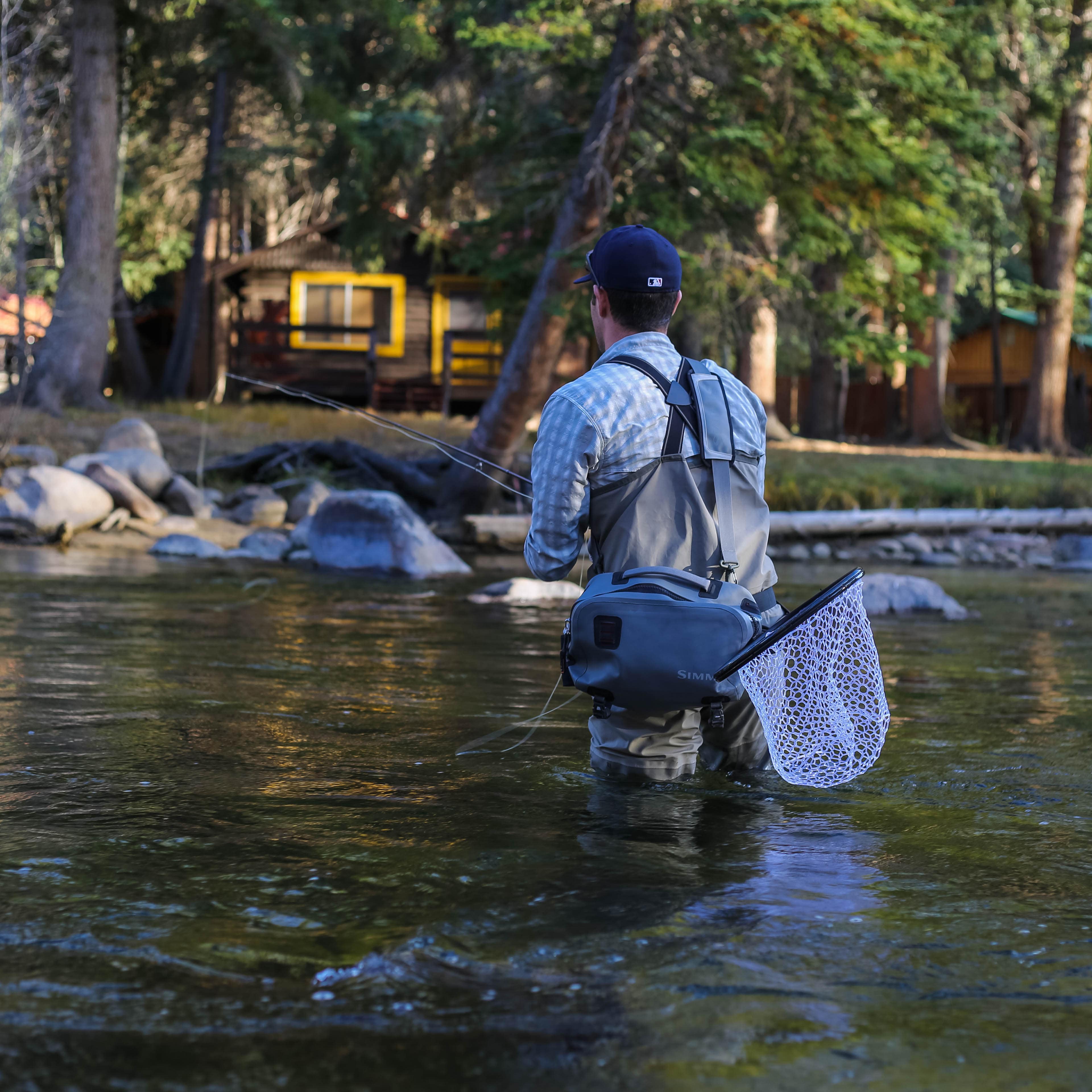 A man in waders fishing in the middle of a river