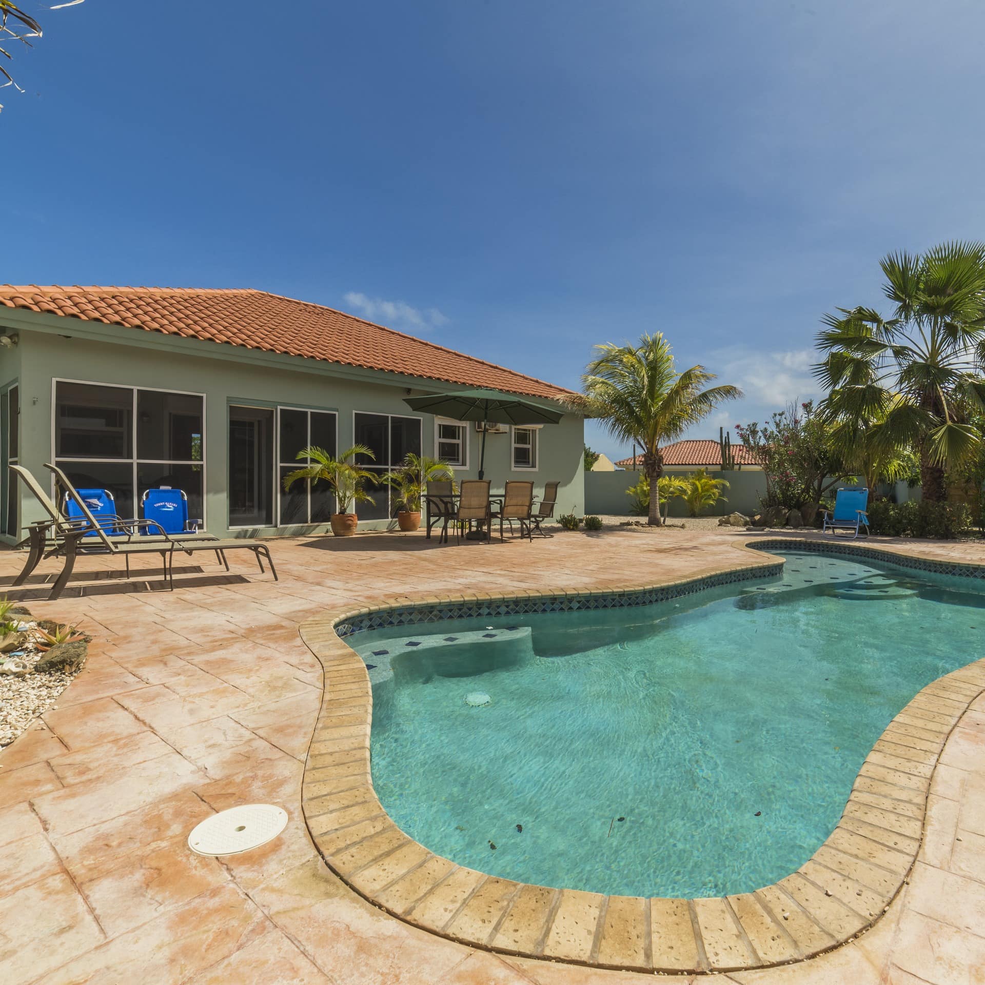 A curvy swimming pool in a paved yard by a luxury villa in Aruba