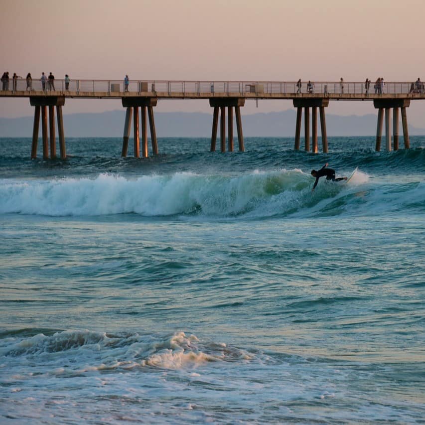 A surfer rides the waves underneath Hermosa Pier