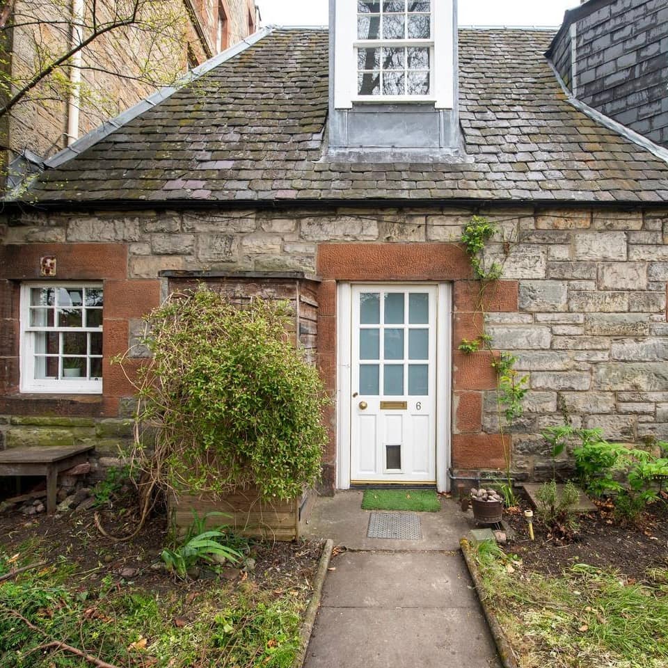 A stone-faced cottage has a path leading to its small white door